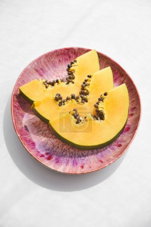 Téléchargez les photos : D'en haut de de papaye exotique fruits avec des graines coupées en morceaux servis sur assiette rose sur fond blanc - en image libre de droit