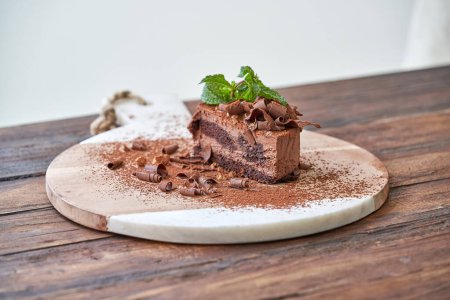 Téléchargez les photos : Délicieux gâteau au chocolat décoré de copeaux et de feuilles de menthe placés sur une planche à découper à table en bois - en image libre de droit