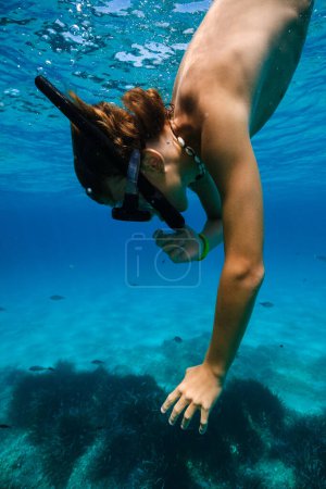 Foto de Vista lateral del niño en máscara de snorkel y tubo de buceo bajo el agua en el mar azul y explorar los fondos marinos con plantas y peces - Imagen libre de derechos