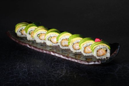 Téléchargez les photos : D'en haut de la rangée de délicieux rouleaux de sushi avec avocat et crevettes sur plaque de marbre placée sur la table sur fond noir - en image libre de droit