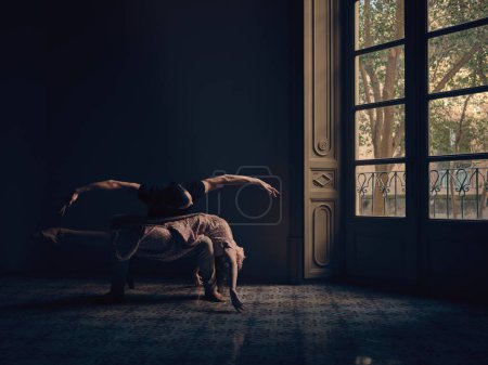 Téléchargez les photos : Corps entier de ballerine couché sur les genoux de l'homme tout en effectuant une danse de ballet près de la fenêtre dans la pièce avec une lumière tamisée - en image libre de droit