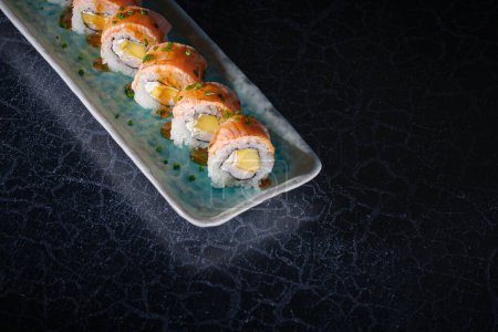 Foto de Deliciosos rollos de sushi uramaki con salmón fresco servidos sobre bandeja de mármol sobre fondo negro - Imagen libre de derechos