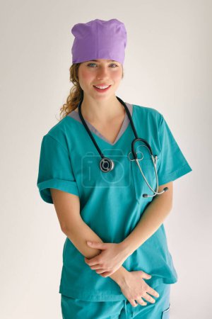 Foto de Señora positiva en ropa de trabajo médica verde y estetoscopio mirando a la cámara mientras está de pie en el estudio - Imagen libre de derechos