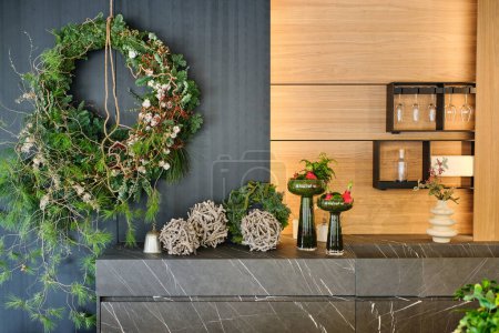 Foto de Corona verde colgando en la pared cerca del mostrador con una variedad de plantas y flores en jarrones colocados en el estudio de floristería moderna - Imagen libre de derechos