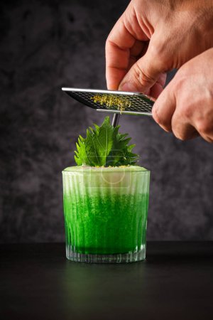 Téléchargez les photos : Cultivez le barman en ajoutant des fleurs de camomille à un cocktail rafraîchissant à l'alcool avec feuille de shiso en utilisant une râpe dans le restaurant - en image libre de droit