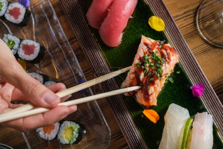 Téléchargez les photos : Vue du dessus de la personne qui mange de savoureux sushi nigiri au saumon cru garni d'oignon vert haché et de sauce soja - en image libre de droit