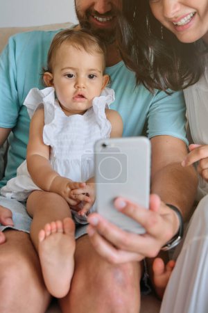 Photo for Crop anonymous parents with daughter watching video on smartphone while spending time at home - Royalty Free Image