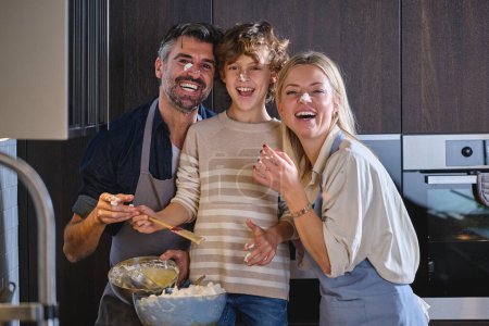Foto de Sonriendo a la gente que se une mientras hace el postre en la cocina acogedora moderna y mirando a la cámara en casa - Imagen libre de derechos