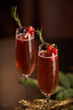 Téléchargez les photos : Verres au champagne alcoolisé décorés de baies de groseilles et de brindilles de romarin servis sur la table avec des boules de Noël pendant les fêtes - en image libre de droit