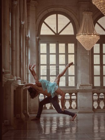 Téléchargez les photos : Vue latérale de la danseuse en pointes levant les bras et la jambe sur le dos partenaire dans le hall spacieux - en image libre de droit