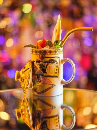 Foto de Bebida larga tropical decorada con hojas de menta servida en taza de cerámica decorada con tapa en la mesa en bar moderno sobre fondo borroso - Imagen libre de derechos