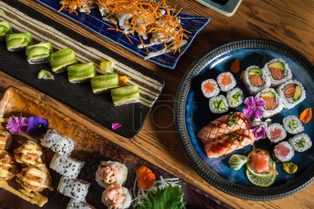 Photo for Top view of delicious sushi rolls with fish and different filling served on tray with decorative flowers and wasabi with ginger - Royalty Free Image