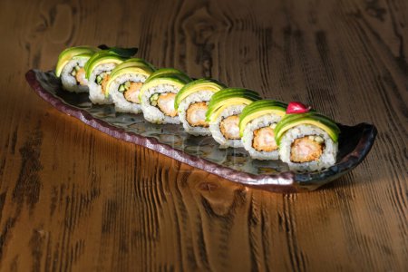 Photo for From above of row of tasty sushi rolls with avocado and shrimp on marble plate placed on wooden table - Royalty Free Image