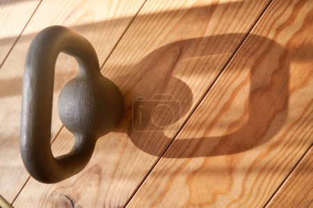Photo for High angle of heavy metal kettlebell with large handle placed on wooden floor in daylight - Royalty Free Image