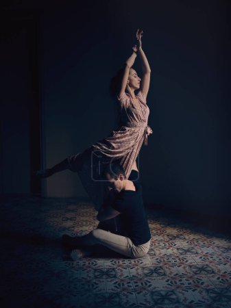 Foto de Vista lateral de cuerpo completo del bailarín masculino que apoya a la bailarina de pie sobre una pierna mientras bailan ballet juntos en un estudio oscuro - Imagen libre de derechos
