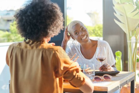 Foto de Optimistic mujer afroamericana sentada frente a un amigo en la mesa en el restaurante y riendo - Imagen libre de derechos