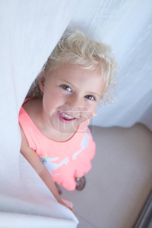 Photo for From above of adorable little girl with blond hair looking at camera while standing in light room at home - Royalty Free Image