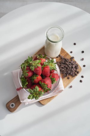 Photo for From above of appetizing fresh strawberries and milk in bottle placed on wooden cutting board with chocolate chips - Royalty Free Image