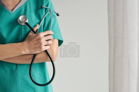 Foto de Doctora en uniforme médico con brazos cruzados y estetoscopio sobre fondo claro - Imagen libre de derechos