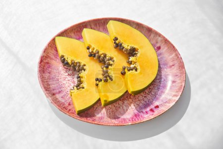 Téléchargez les photos : Angle élevé de portion de savoureux fruits exotiques de papaye avec des graines coupées en morceaux servis sur une assiette en céramique rose sur fond blanc - en image libre de droit