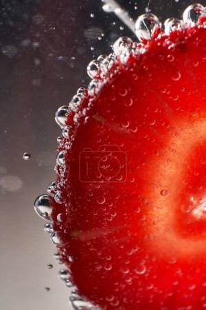 Foto de Primer plano pedazo de fresa fresca cubierta con burbujas transparentes en vaso de bebida fría - Imagen libre de derechos
