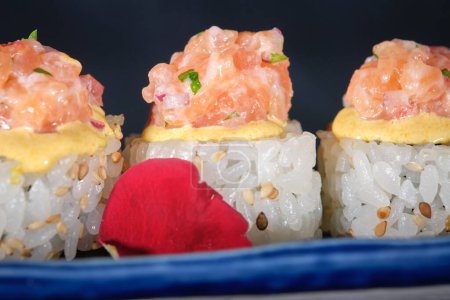 Téléchargez les photos : Gros plan de sushis appétissants garnis de saumon et de sauce fraîche servis sur un plateau bleu posé sur la table du restaurant sur fond noir - en image libre de droit