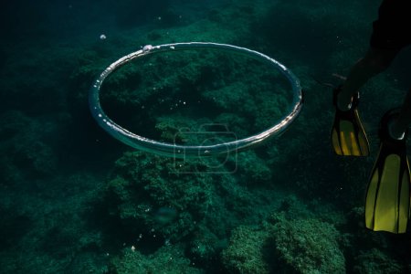 Foto de Inyección submarina de gran anillo de burbujas cerca de buceador anónimo en aletas nadando en aguas profundas - Imagen libre de derechos