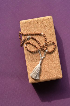 Photo for From above of rosary beads placed on wooden yoga block on sports mat prepared for practice - Royalty Free Image