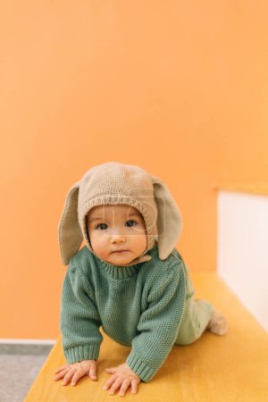 Photo for Full body of adorable cute baby in warm clothes and hat with bunny ears sitting on stairs - Royalty Free Image