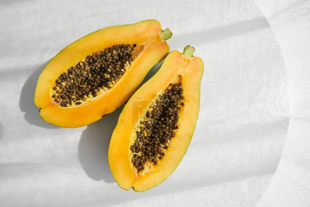 Téléchargez les photos : D'en haut des moitiés fraîches de papaye jaune mûre biologique avec des graines placées sur la table grise au soleil en studio - en image libre de droit