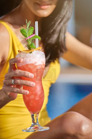 Photo for Crop anonymous female in yellow swimsuit with glass of fresh cocktail with lemon and mint leaves on blurred background - Royalty Free Image