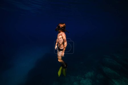 Foto de Vista lateral de adolescente sin camisa niño en aletas y buceo máscara de snorkel bajo el agua azul oscuro de mar profundo durante las vacaciones - Imagen libre de derechos