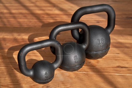 Téléchargez les photos : Grand angle de lourdes cloches de kettlebells de différents poids organisés en rangée et placés sur le parquet dans la salle de gym - en image libre de droit