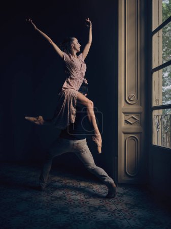 Photo for Full body side view of anonymous talented male dancer carrying graceful ballerina on shoulder while dancing ballet dance together in obscure room - Royalty Free Image