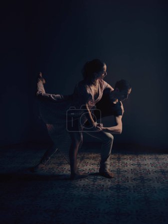 Foto de Vista lateral de cuerpo completo del talentoso activo hombre y mujer descalzos realizando movimiento de danza de ballet en el estudio con poca luz - Imagen libre de derechos