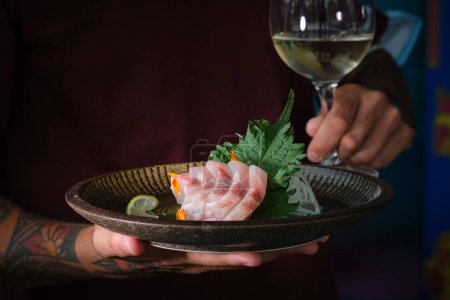 Foto de Camarero masculino anónimo de cultivo que sirve sashimi de lubina fresca con vino blanco en el restaurante sobre fondo borroso - Imagen libre de derechos