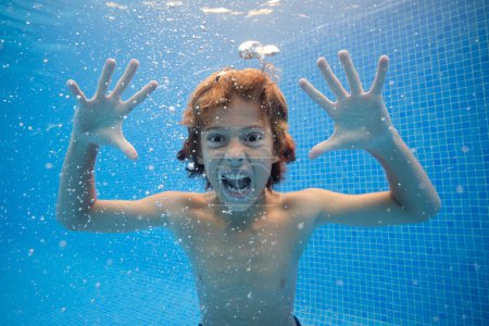 Téléchargez les photos : Garçon avec la bouche ouverte criant avec les yeux grands ouverts dans l'eau claire de la piscine et regardant la caméra - en image libre de droit