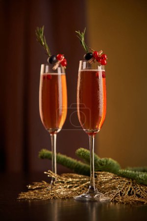 Téléchargez les photos : Verres de champagne décorés de baies et de brindilles de romarin placés sur une table décorée avec des branches de conifères dans la chambre lors d'un événement festif - en image libre de droit