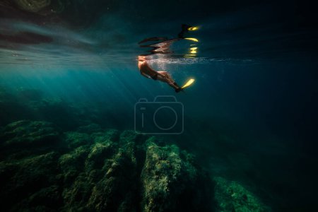 Foto de Vista lateral de buzo masculino anónimo en aleta nadando bajo agua azul de mar profundo cerca de arrecifes de coral ásperos - Imagen libre de derechos
