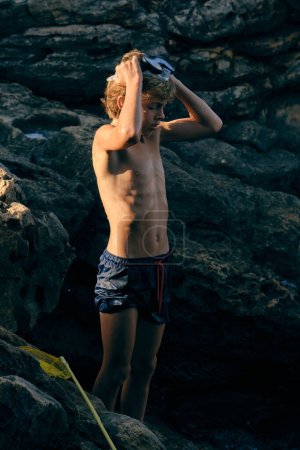 Téléchargez les photos : Enfant dans des maillots de bain portant des lunettes de plongée debout sur le mont dans les rayons du soleil - en image libre de droit