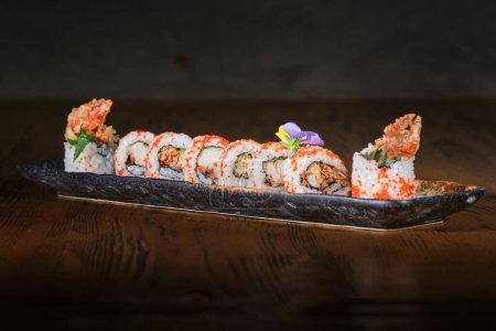 Foto de Set servido de sushi uramaki japonés con huevas de pescado tobiko rojo y garras de cangrejo fritas tempura en mesa de madera - Imagen libre de derechos