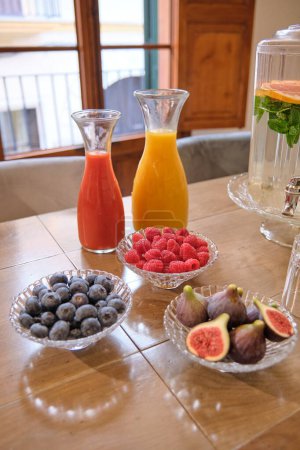 Téléchargez les photos : Buffet de figues douces framboises bleuets et boissons santé sucrées servies en verrerie sur table en bois dans la salle de réunion lumineuse - en image libre de droit