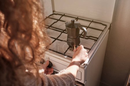 Photo for From above of crop anonymous woman with curly hair lighting gas stove while preparing coffee in metal geyser coffeemaker in kitchen - Royalty Free Image