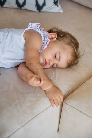 Téléchargez les photos : D'en haut de adorable petite fille couchée sur un canapé confortable et dormant dans le salon à la maison - en image libre de droit