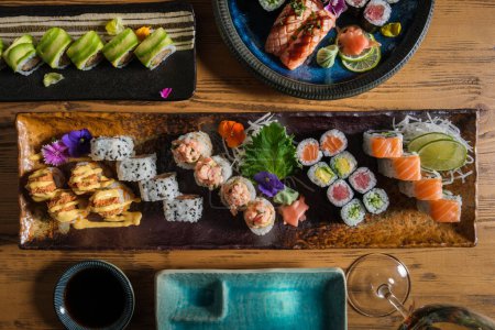 Foto de Vista superior de surtidos rollos de sushi fresco servidos en bandejas en mesa de madera con vino y salsa de soja en la cafetería - Imagen libre de derechos