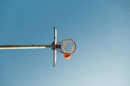 Téléchargez les photos : De dessous de panier de basket avec filet sur anneau et boule orange contre ciel clair sans nuages - en image libre de droit