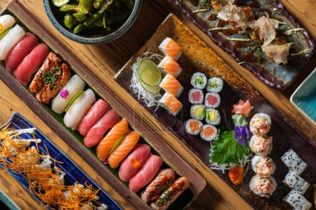 Photo for Top view of various fresh sushi and rolls with different fish served on wooden trays with shrimps in light cafe - Royalty Free Image