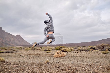 Téléchargez les photos : Vue de l'arrière du corps entier mâle anonyme en vêtements de sport sautant sur un terrain pierreux sec près du volcan Teide à Tenerife dans les îles Canaries en Espagne - en image libre de droit