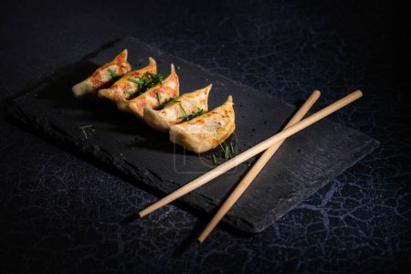 Photo for High angle of delicious fried gyoza with crispy dough topped with chopped chives on black slate board near crossed chopsticks - Royalty Free Image