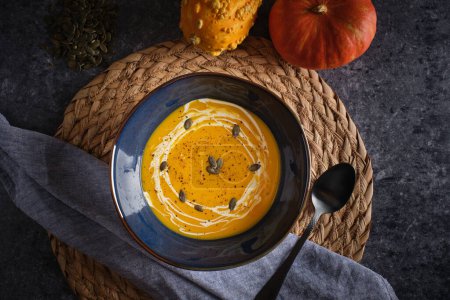 Photo for Top view of delicious squash puree soup with seeds placed on black table with napkin and spoon - Royalty Free Image